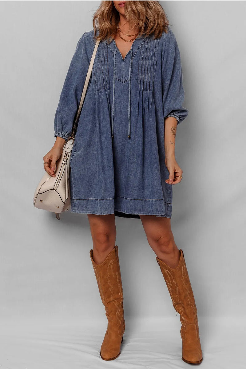 Woman wearing a blue denim dress and brown knee-high boots against a plain background