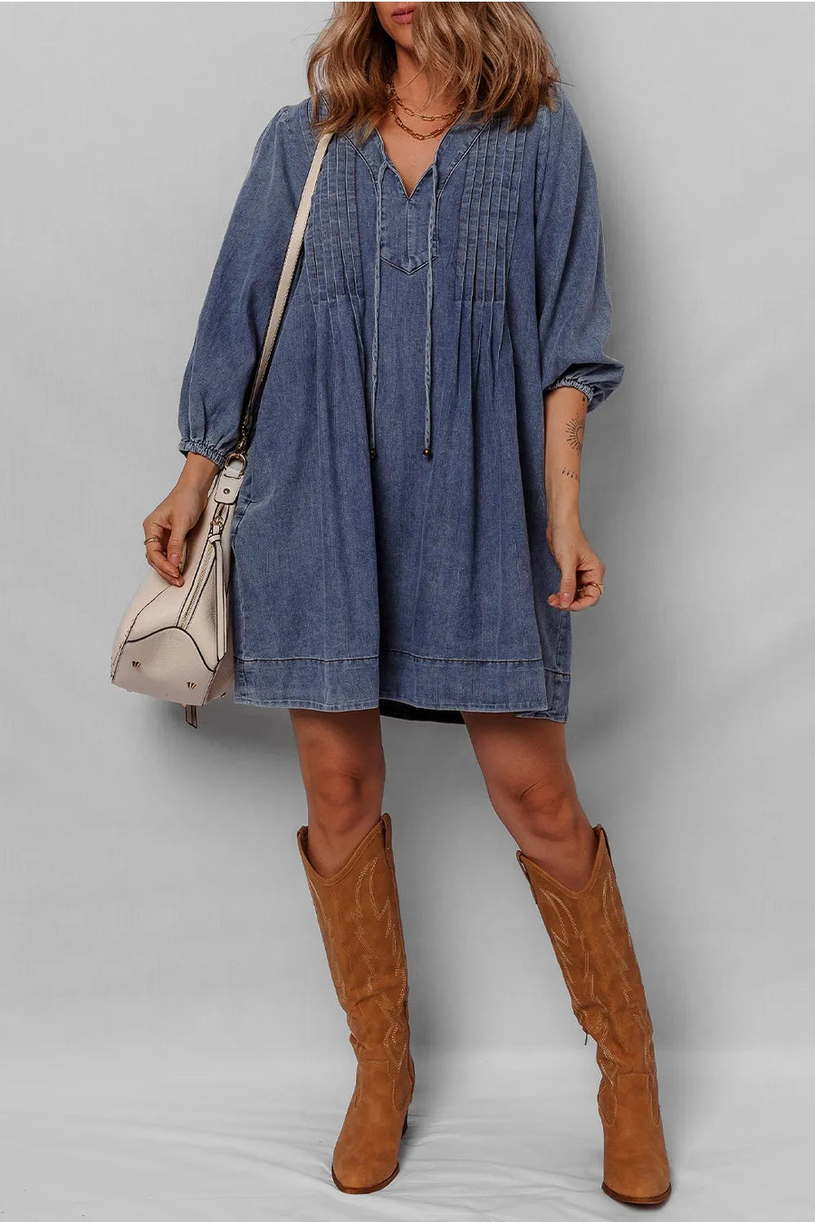Woman wearing a blue denim dress and brown knee-high boots against a plain background