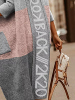 Person wearing a patterned cardigan with text, holding a small handbag.