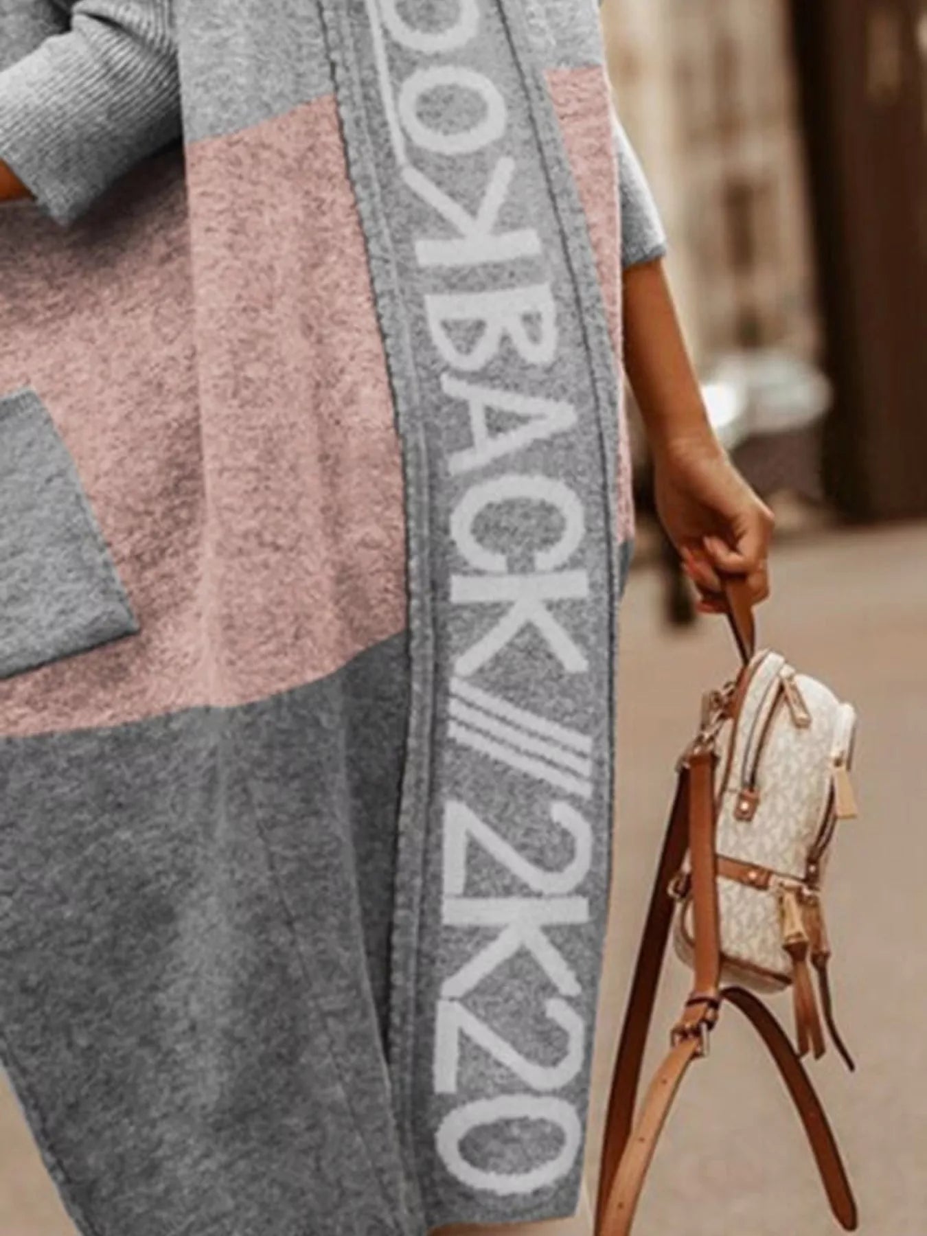 Person wearing a patterned cardigan with text, holding a small handbag.