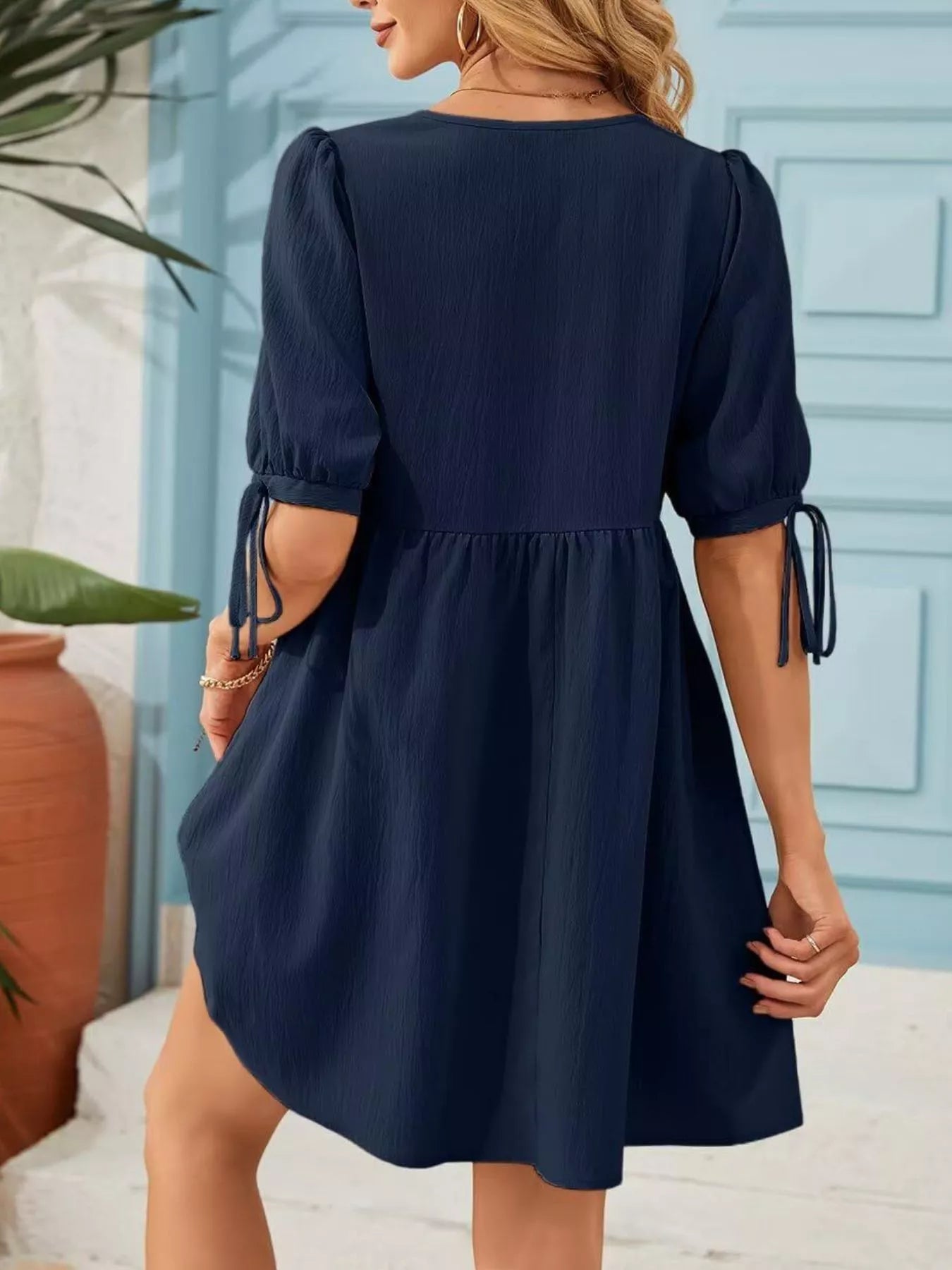 Navy blue dress with puff sleeves worn by a person, standing against a light blue wall.