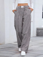 Person wearing black and white checkered pants with a white top and shoes on a stone pavement.