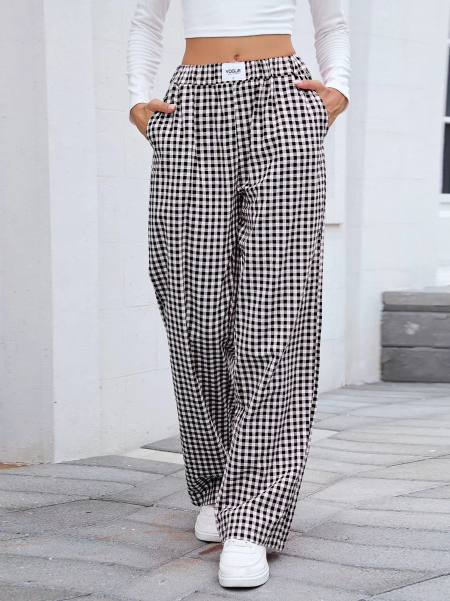 Person wearing black and white checkered pants with a white top and shoes on a stone pavement.