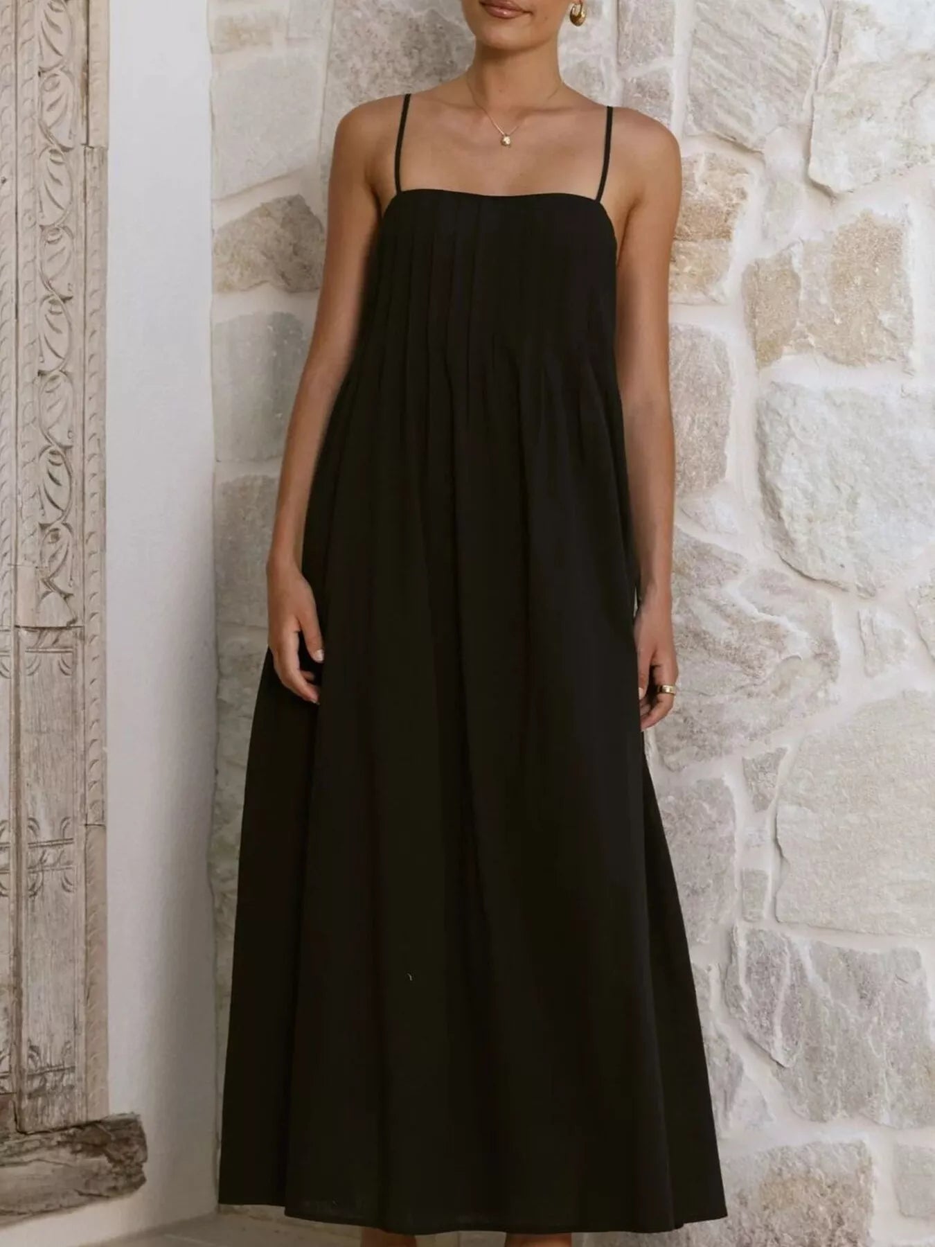 Woman wearing a black dress against a stone wall.