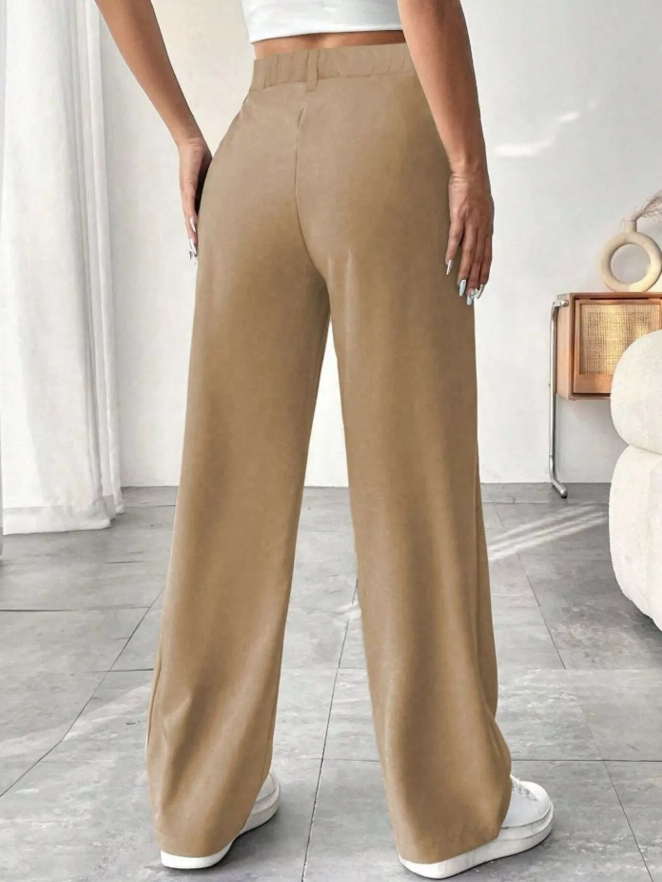 Person wearing beige wide-leg pants in a room with a white wall and gray floor.