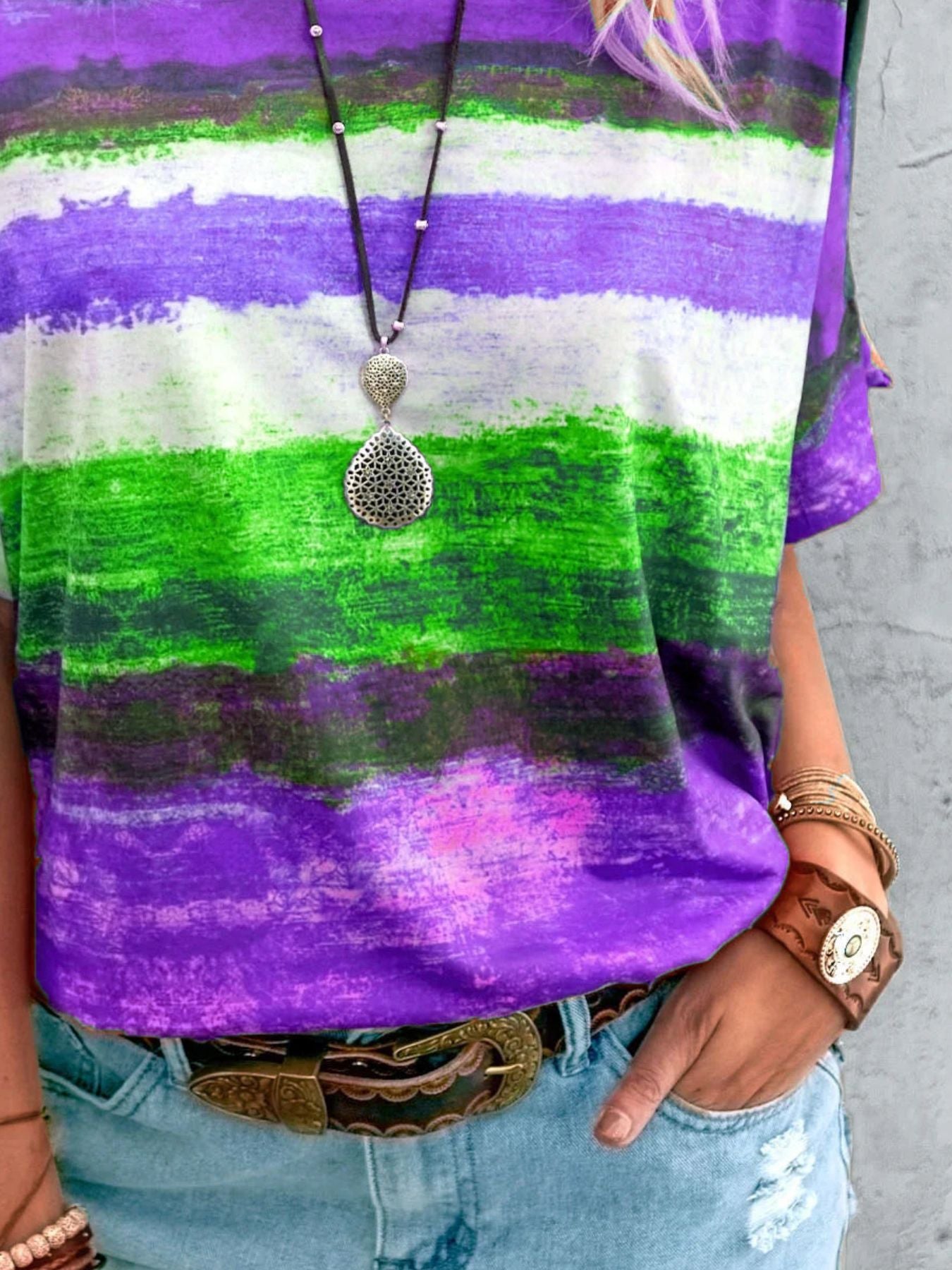 Person wearing a colorful striped shirt with a pendant necklace and bracelets.