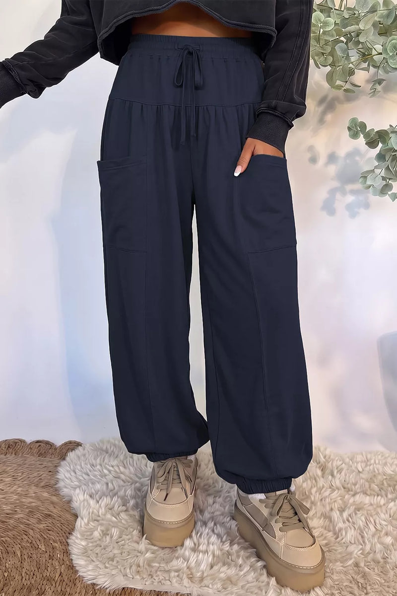 A person wearing loose navy drawstring pants with side pockets, paired with beige platform sneakers, standing indoors on a white shag rug.
