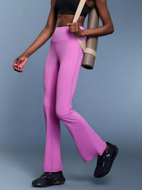 Person wearing pink leggings and black shoes holding a yoga mat on a blue background