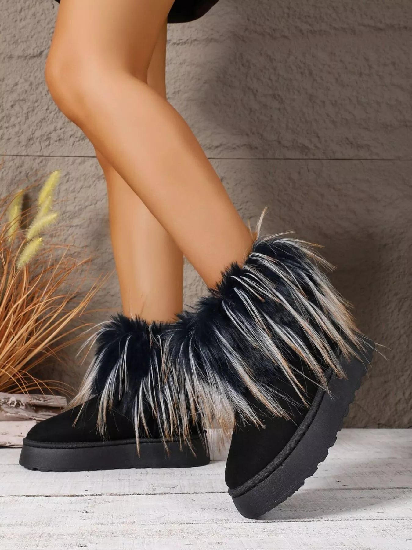 Black fuzzy boots with fur trim worn by a person, against a neutral background.