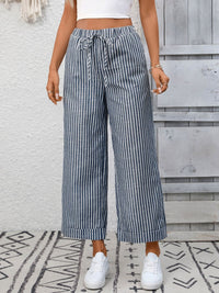 Person wearing blue and white striped wide-leg pants with a white top and white sneakers, standing on a patterned rug.