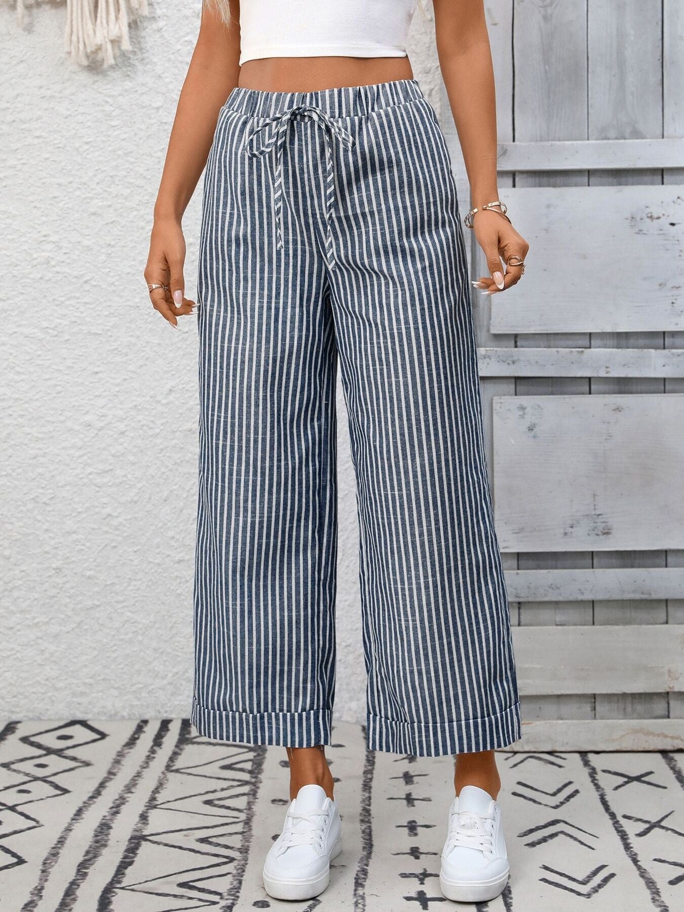 Person wearing blue and white striped wide-leg pants with a white top and white sneakers, standing on a patterned rug.