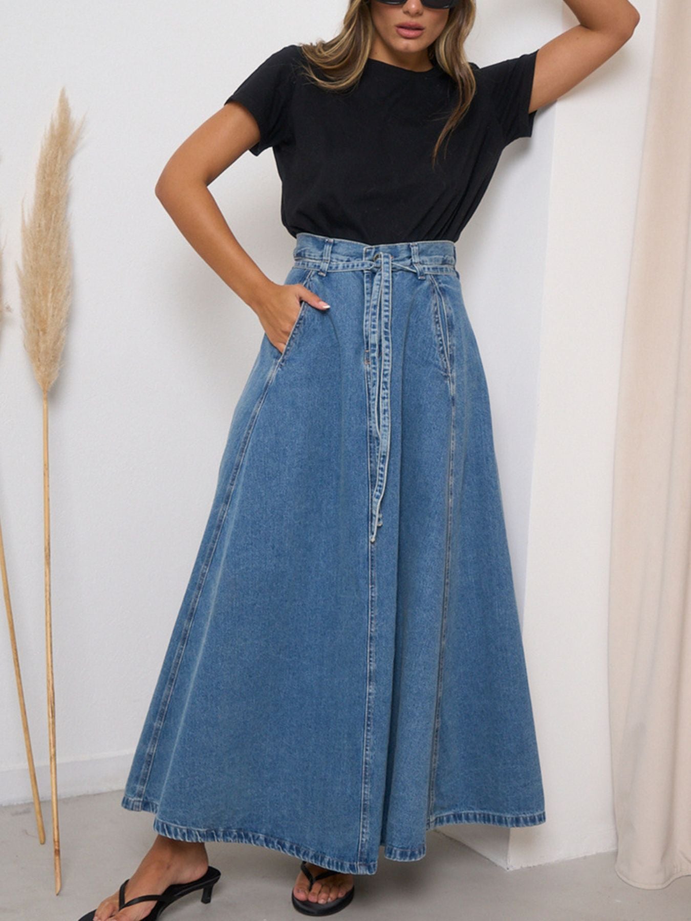 Person wearing a black t-shirt and blue denim skirt against a white wall.
