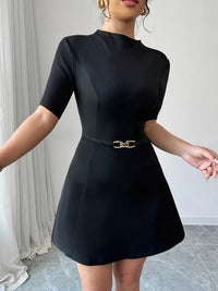 Black dress with a belt worn by a person against a neutral background