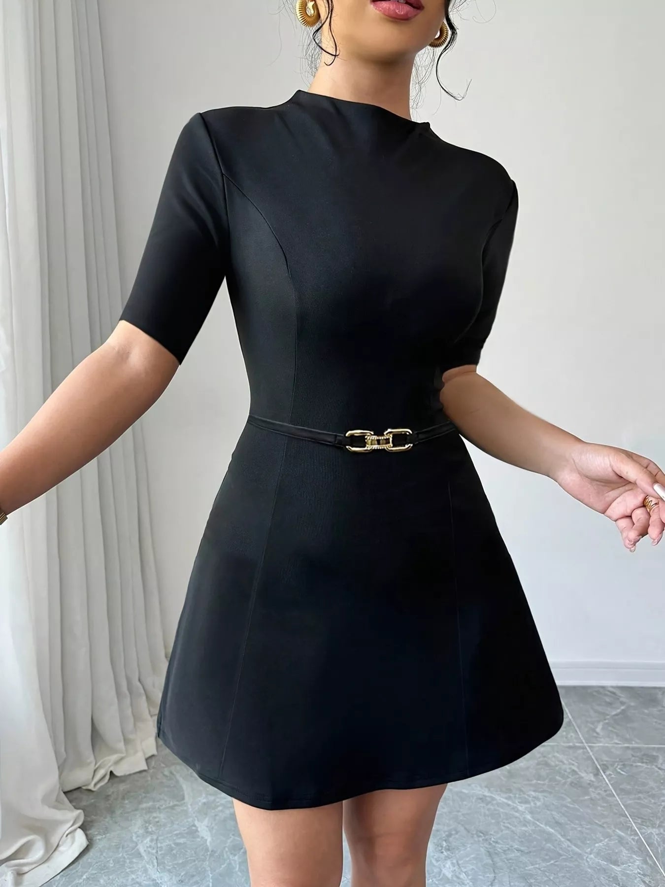 Black dress with a belt worn by a person against a neutral background