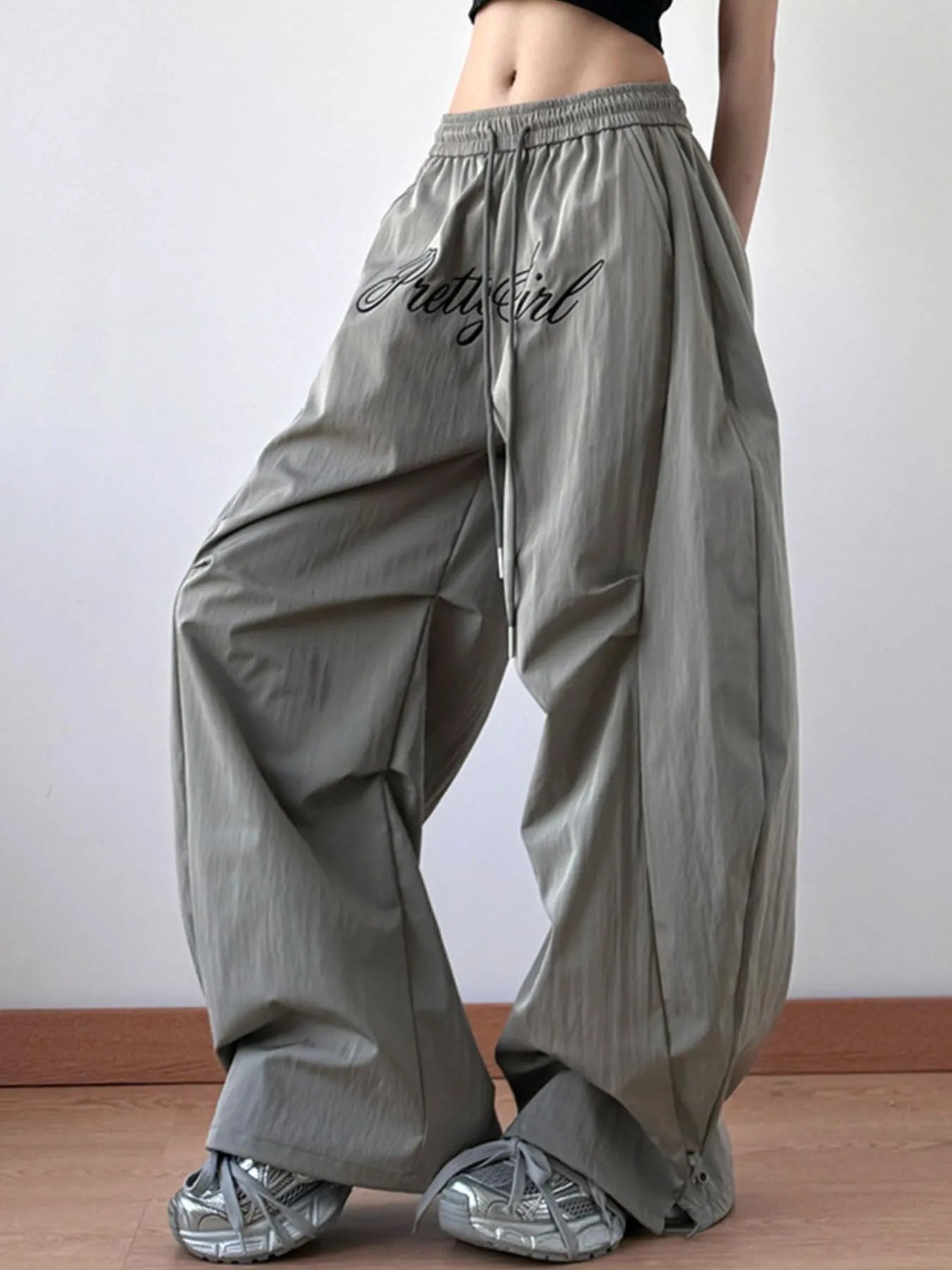 Person wearing gray wide-leg pants with 'Pretty Girl' text on a plain background