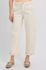 Person wearing light-colored jeans and beige shoes on a plain background