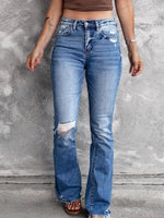 Person wearing blue distressed jeans against a gray concrete wall.