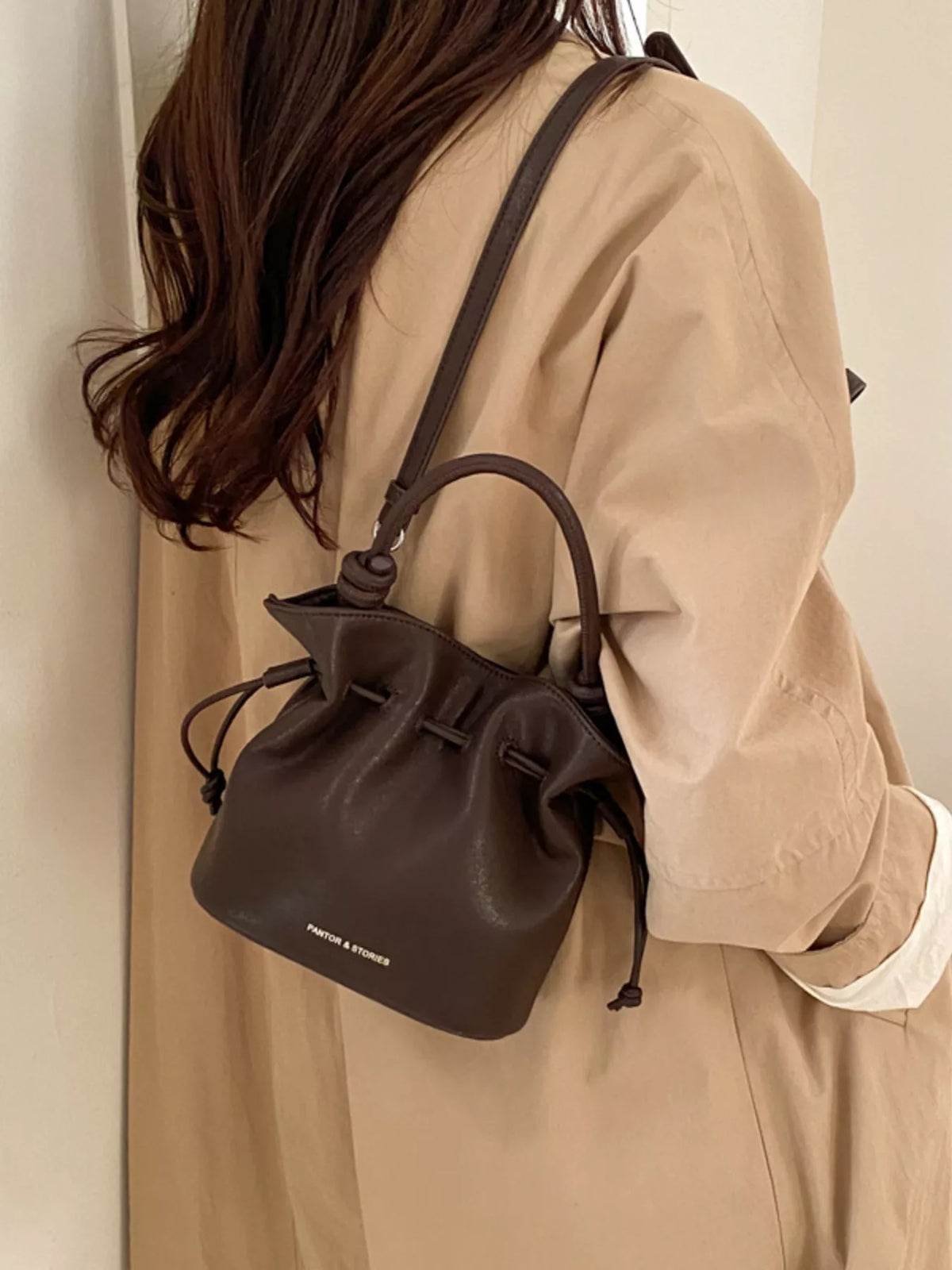 Person wearing a brown leather drawstring bag over their shoulder against a neutral background