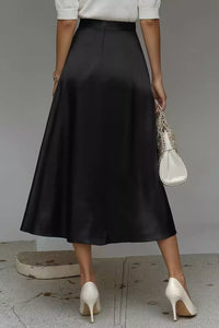 Person wearing a black skirt with white shoes and a white top, holding a white handbag.