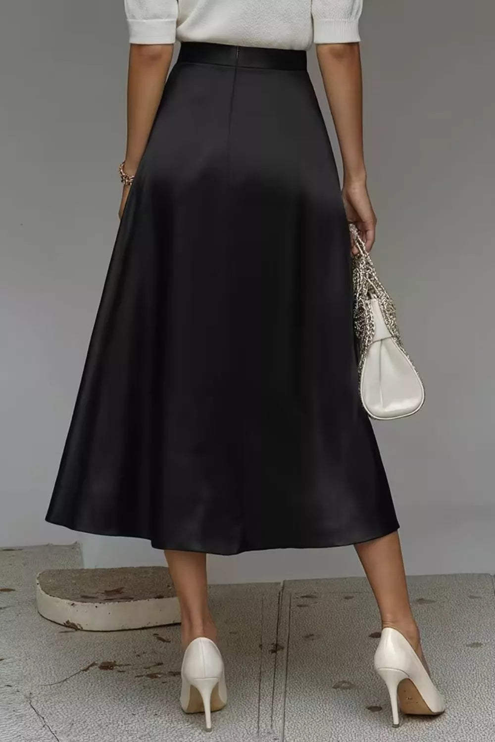 Person wearing a black skirt with white shoes and a white top, holding a white handbag.