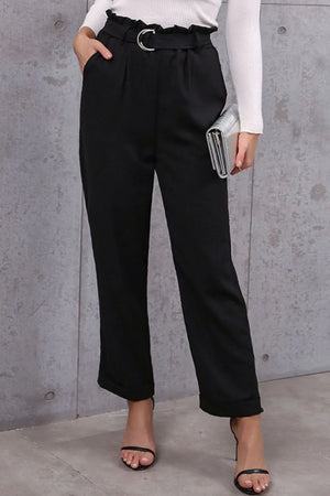 Person wearing black high-waisted pants with a belt against a gray concrete wall.