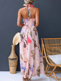 Woman wearing a floral dress standing in front of a dark wall with a vase and chair.