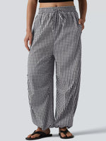 A person wearing loose black-and-white gingham drawstring pants with side pockets, shown from the waist down against a light gray studio background.