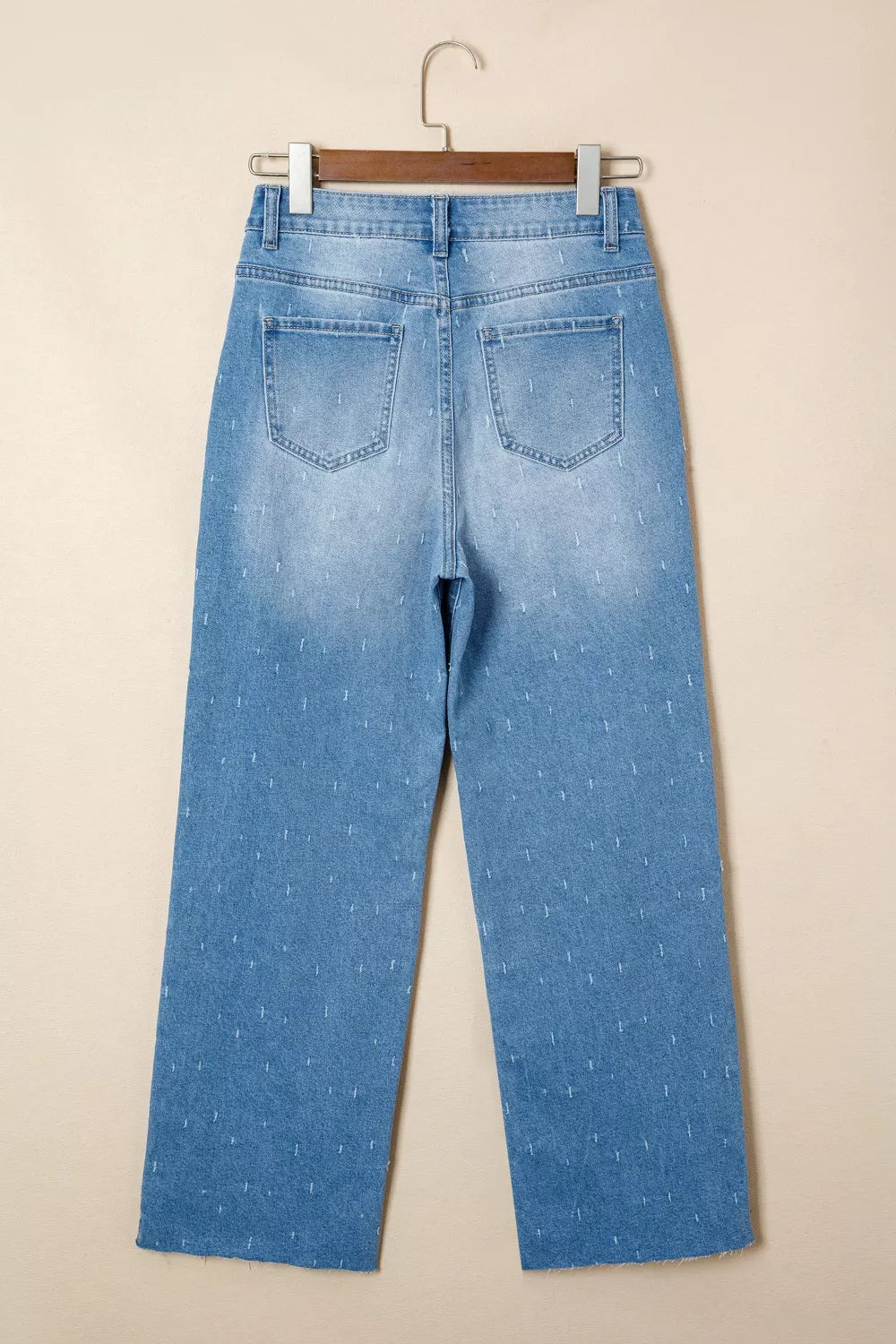 Light blue jeans on a hanger against a beige background