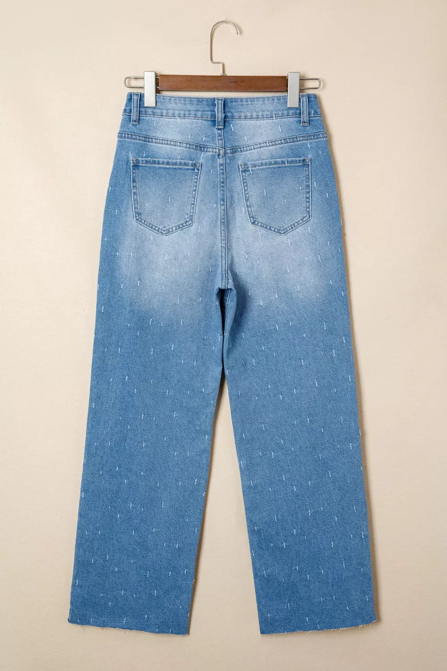 Light blue jeans on a hanger against a beige background