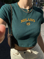 Person wearing a green t-shirt with 'Milano 95' print, holding a phone.