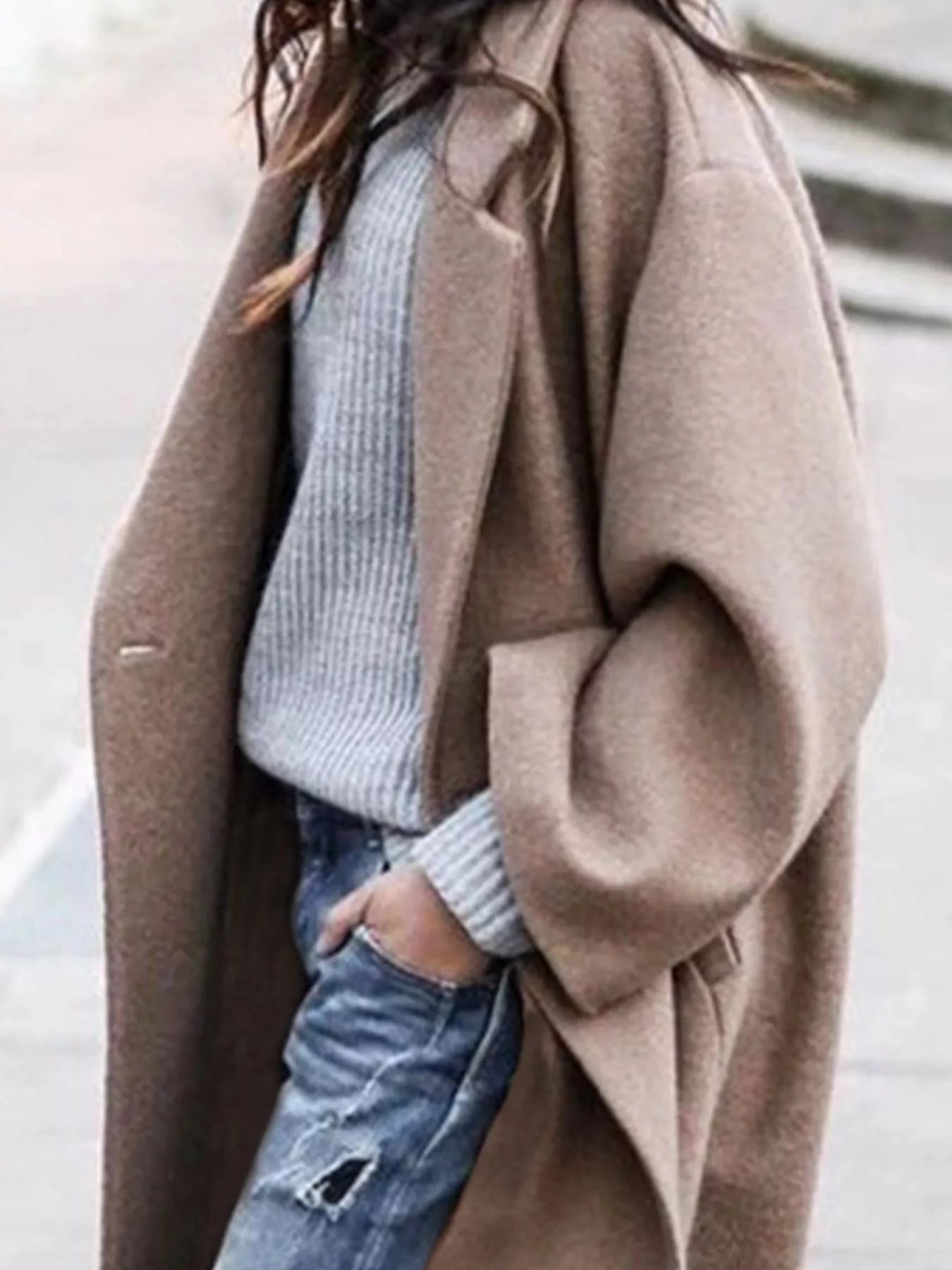 Person wearing a beige coat over a light blue sweater and jeans.