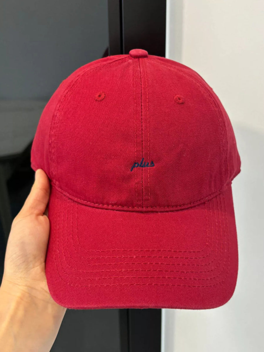 Red cap held by a hand with a brand logo on a neutral background