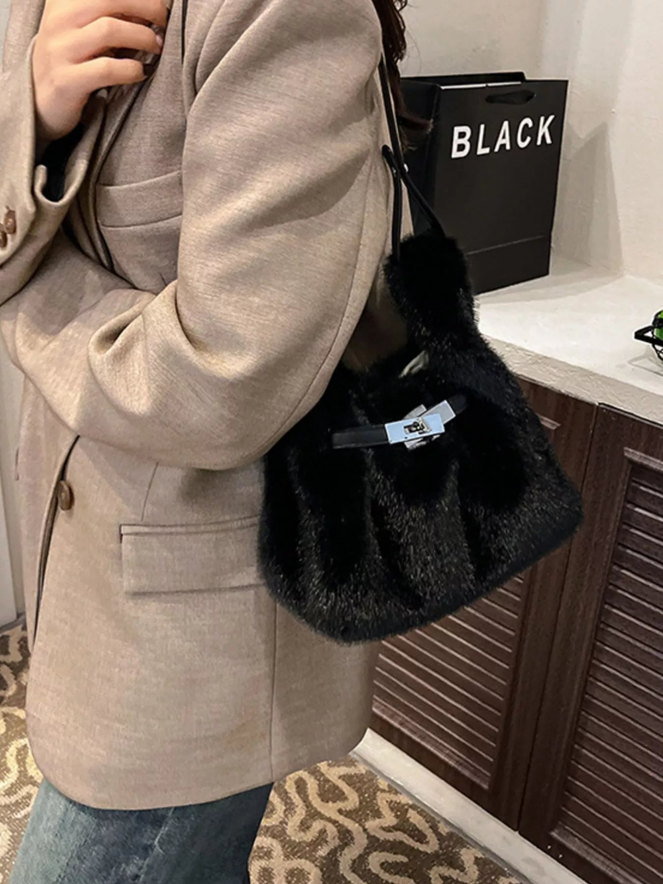 Person holding a black handbag with a visible brand logo, standing indoors.