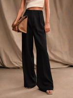 Person wearing black wide-leg pants holding a beige clutch against a neutral background