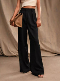 Person wearing black wide-leg pants holding a beige clutch against a neutral background