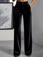 Black velvet wide-leg pants with a high waist and front pleats, shown on a model in a minimalist studio setting.