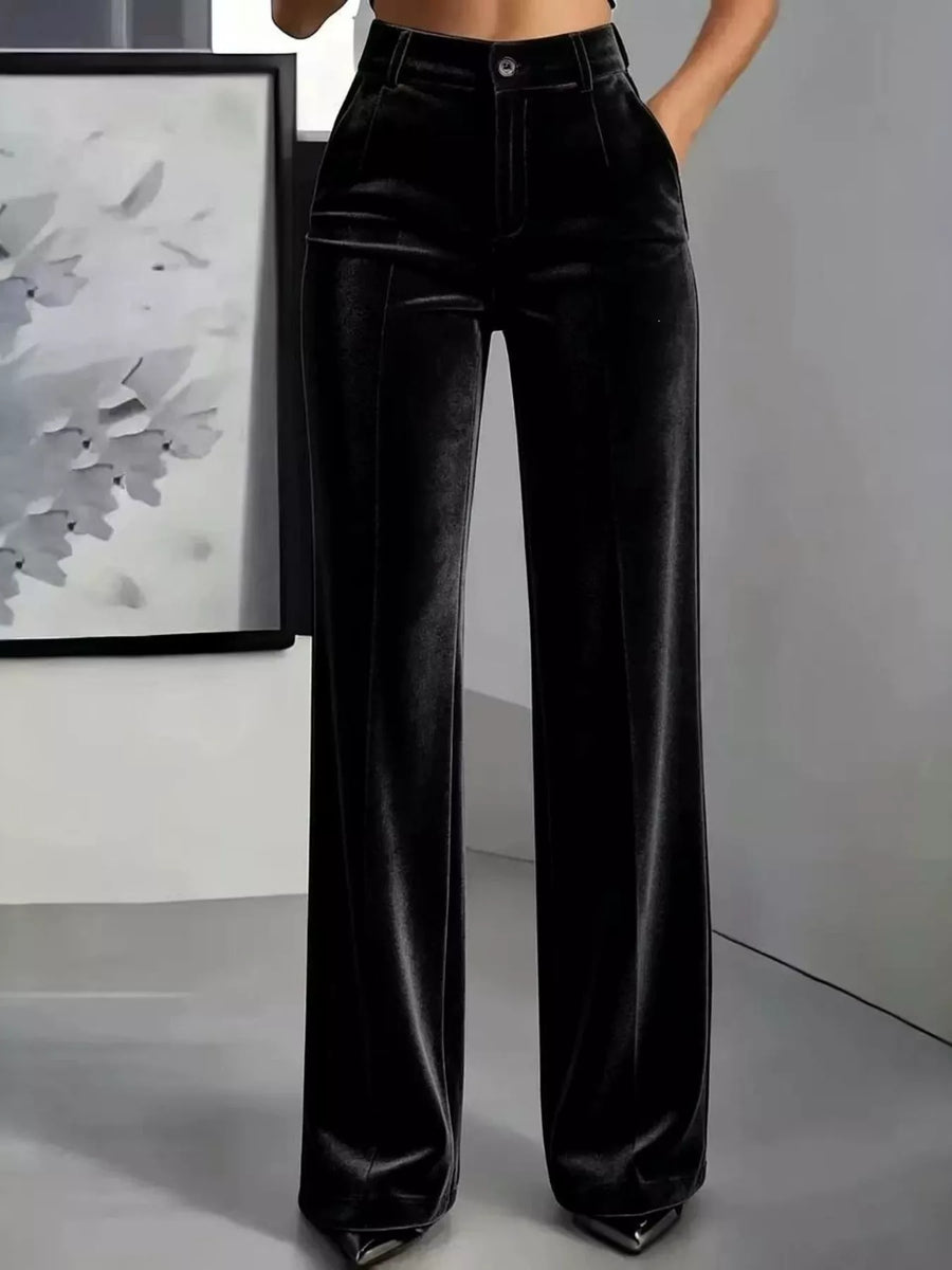 Black velvet wide-leg pants with a high waist and front pleats, shown on a model in a minimalist studio setting.