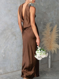 Woman in a brown dress holding flowers against a textured wall.
