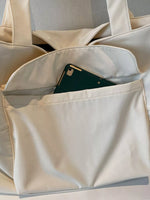 Beige tote bag with a green phone inside on a light gray background