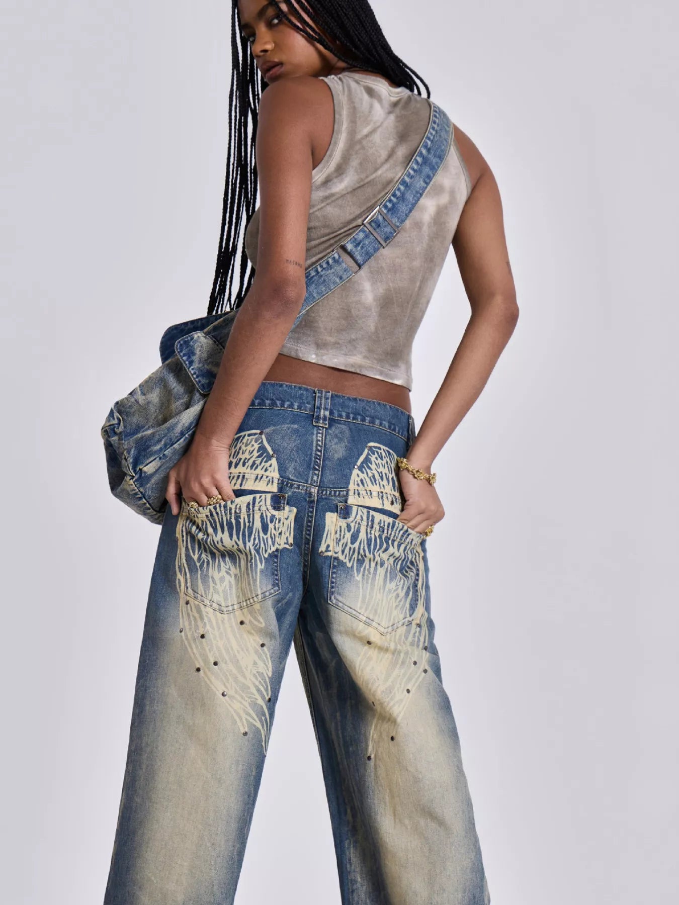 Person wearing a sleeveless denim top and distressed jeans on a plain background