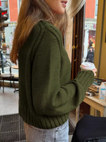 Person wearing a green sweater holding a coffee cup in an urban setting.