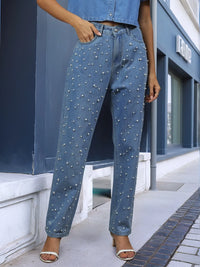 Person wearing studded blue jeans standing on a sidewalk.