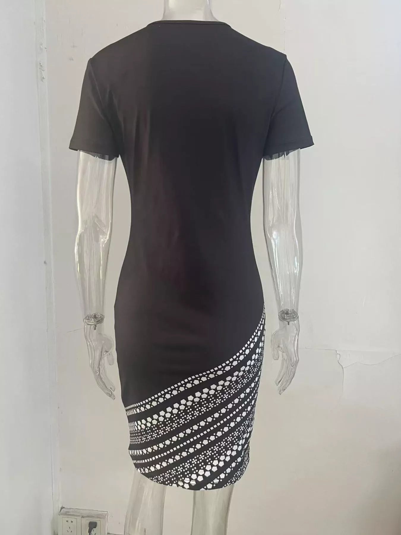 Black dress with white patterned hem on a mannequin against a white background