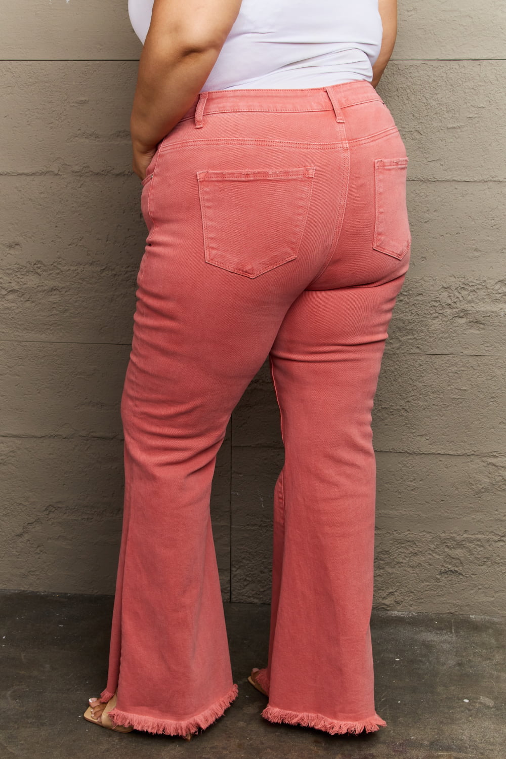 Person wearing pink flared jeans against a gray wall.