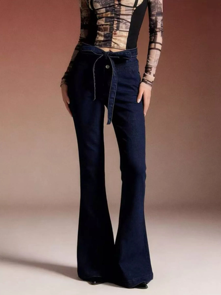 Person wearing a patterned top and dark blue flared jeans on a beige background