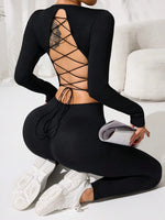 Person wearing a black open-back top and leggings with white sneakers, sitting on a white couch.