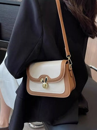 Person wearing a white and brown handbag with a gold clasp.