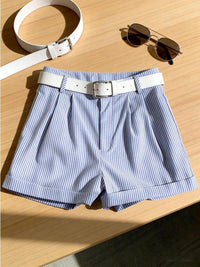 Blue and white striped shorts with a white belt and sunglasses on a wooden surface