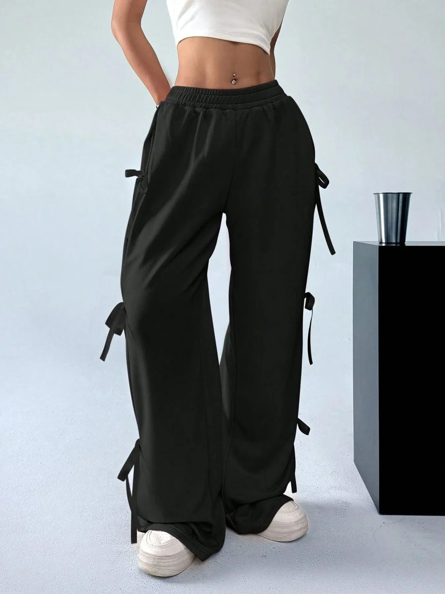 Black wide-leg pants with tie details worn by a person on a light blue background