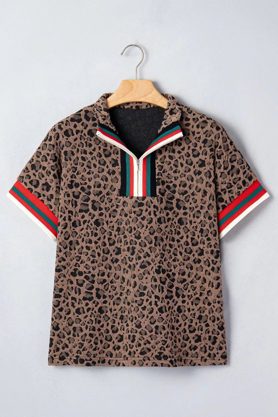 Leopard print polo shirt with red and green stripes on a hanger against a light gray background
